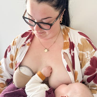 Woman breastfeeding a baby wrapped in a purple blanket against a neutral background